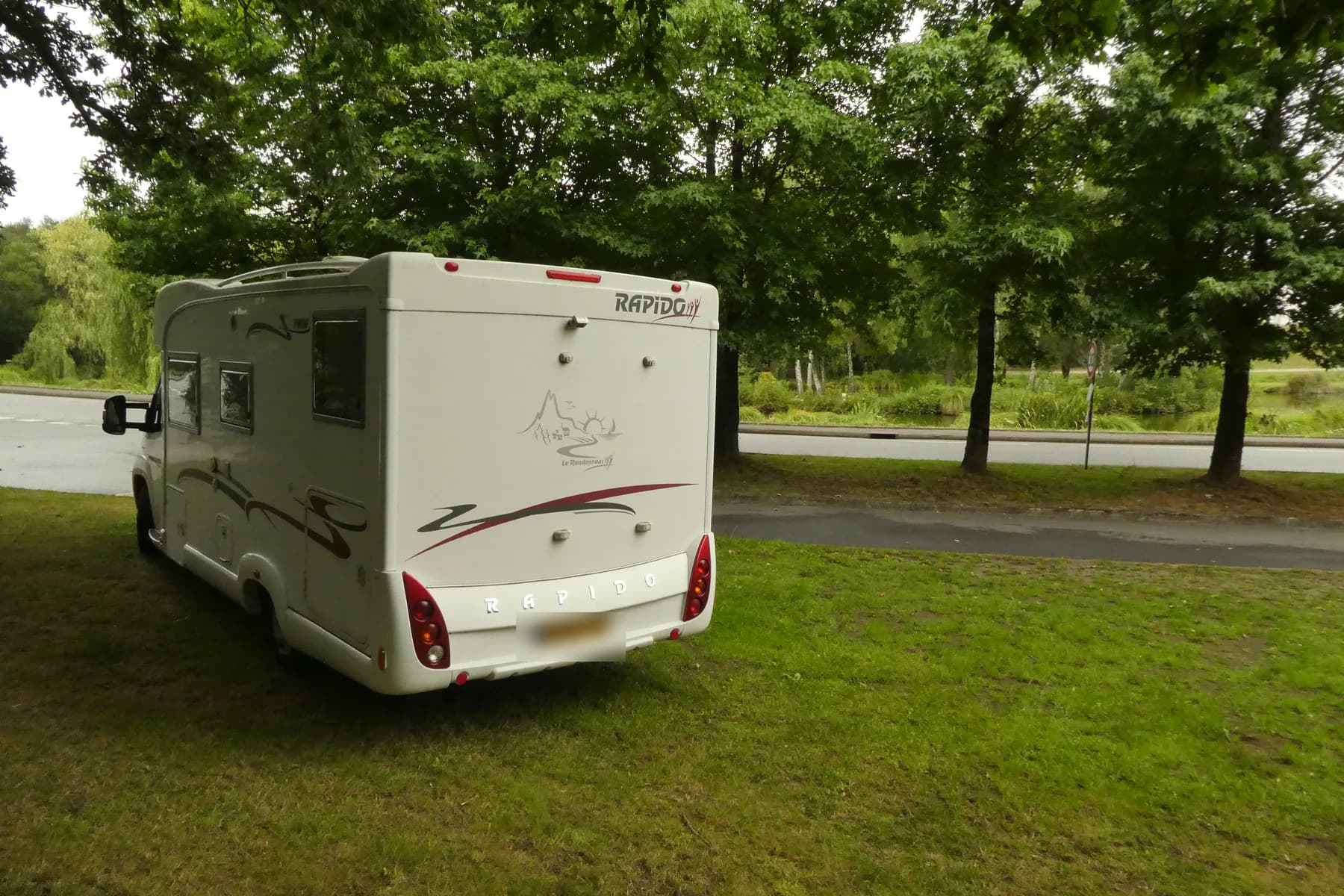 A UK-registered Rapido motorhome parked on grass beside trees on a French aire