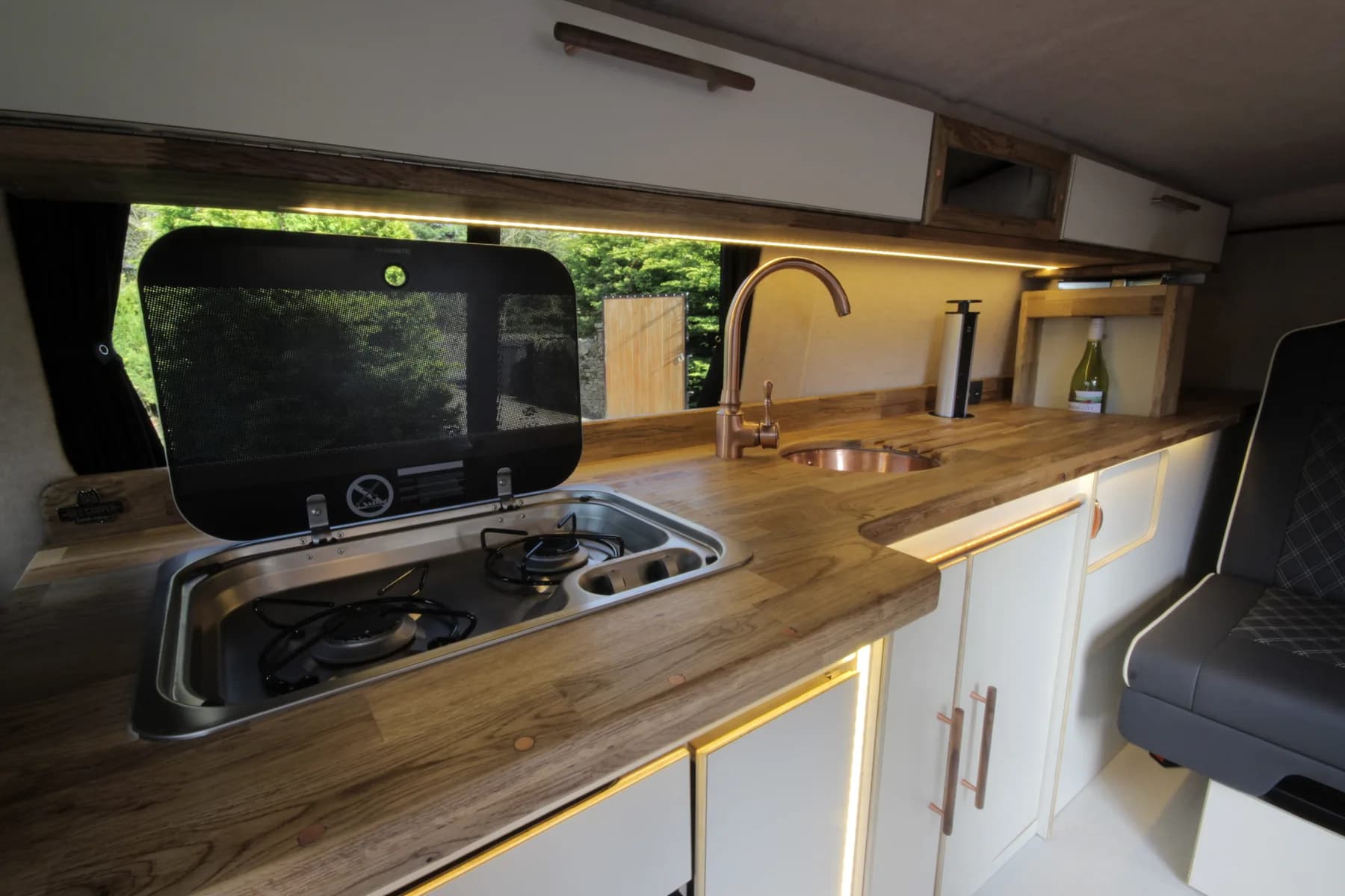 Interior of a self-built Volkswagen campervan with a small kitchen and LED strip lighting